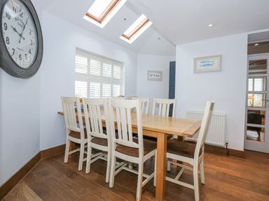 A dining room with a wooden table and eight white chairs under skylights at Min Y Mor - Morfa Nefyn