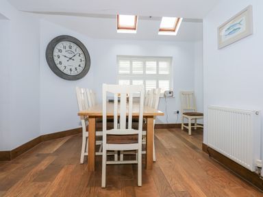 A dining room with a wooden table and chairs a large wall clock and a window with shutters at Min Y Mor - Morfa Nefyn in Morfa Nefyn
