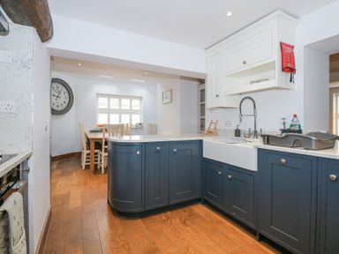 A kitchen with blue cabinets a white countertop and a dining table with chairs at Min Y Mor - Morfa Nefyn