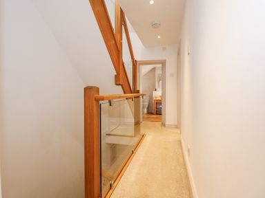 A hallway with carpet flooring and wooden handrails leading to a bathroom at Min Y Mor - Morfa Nefyn