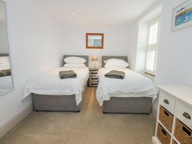 A bedroom with two single beds a small bedside table lamp mirror and a window with shutters at Min Y Mor - Morfa Nefyn