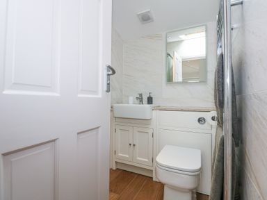 A small bathroom with a white door a sink with a cabinet a toilet a mirror and a heated towel rail at Min Y Mor - Morfa Nefyn