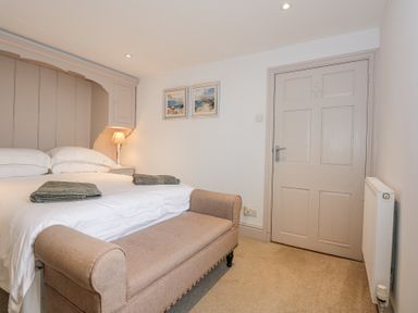 A bedroom with a bed folded towels a bench two paintings on the wall and a closed door at Min Y Mor - Morfa Nefyn
