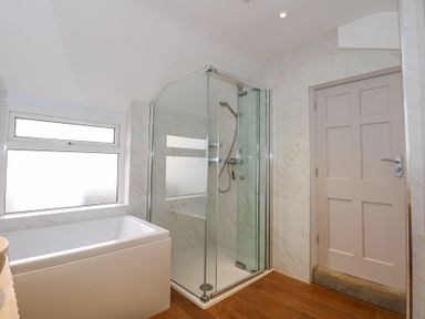 A bathroom with a bathtub, glass enclosed shower, wooden floor, and a closed door at Min Y Mor - Morfa Nefyn