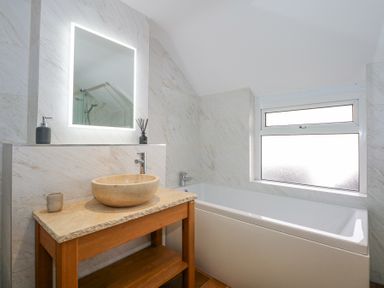 A bathroom with a stone sink on a wooden vanity and a bathtub next to a frosted window at Min Y Mor - Morfa Nefyn