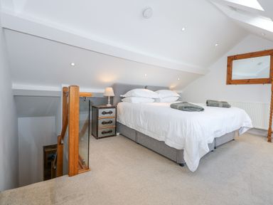 A bedroom with a bed and bedside table next to stairs and a wooden framed mirror at Min Y Mor - Morfa Nefyn