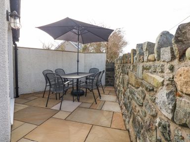An outdoor patio with a table, six chairs, and a large umbrella next to a stone wall at Min Y Mor - Morfa Nefyn