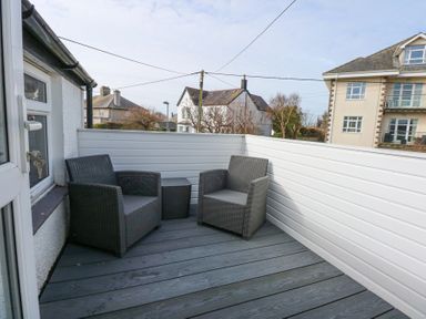 An outdoor balcony with two wicker chairs and a small table at Min Y Mor - Morfa Nefyn
