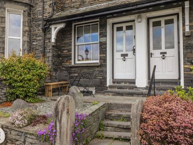 Front entrance of a cottage with two white doors stone steps stone walls and flower bushes at Primrose Cottage Ambleside