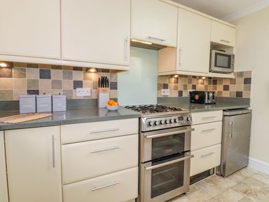 A kitchen with white cabinets a gas stove a microwave a toaster and containers labeled coffee sugar and tea at Primrose Cottage in Ambleside