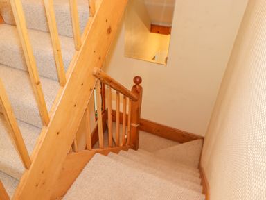 A carpeted staircase with wooden banisters and a mirror on the wall at Primrose Cottage in Ambleside