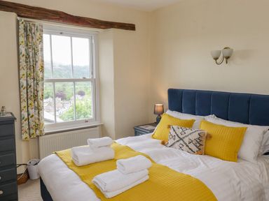 A bedroom with a bed with yellow and white bedding near a window with floral curtains at Primrose Cottage in Ambleside