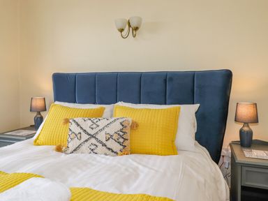A bedroom with a blue headboard yellow and white pillows bedside tables with lamps on at Primrose Cottage Ambleside