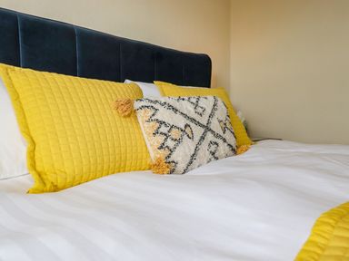 A bed with a dark headboard white bedding and yellow and patterned pillows at Primrose Cottage in Ambleside