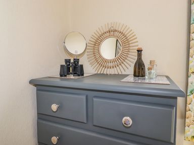 A gray dresser with a round mirror frame binoculars and glass bottles on top at Primrose Cottage Ambleside
