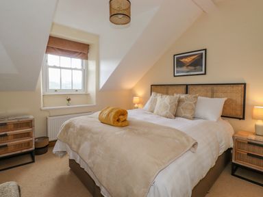 A bedroom with a bed with pillows and a folded yellow blanket a window and wooden furniture at Primrose Cottage in Ambleside