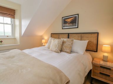 A bedroom with a bed with multiple pillows bedside tables with lamps and a window at Primrose Cottage in Ambleside