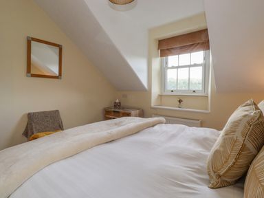 A bedroom with a bed pillows a window a wooden bedside table a chair and a wall mirror at Primrose Cottage in Ambleside