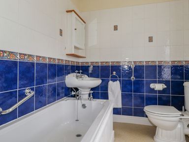 A bathroom with a bathtub sink toilet and blue and white tiled walls at Primrose Cottage in Ambleside
