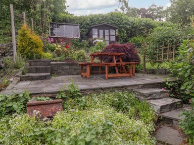 A garden with stone steps wooden picnic table shed and plants at Primrose Cottage Ambleside