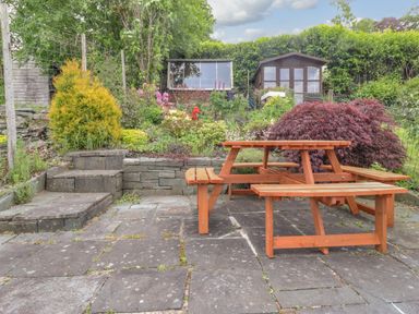 An outdoor patio with a wooden picnic table stone steps and garden sheds at Primrose Cottage in Ambleside