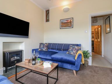 A living room with a blue sofa a wooden coffee table with books and drinks and a wall-mounted TV at Primrose Cottage in Ambleside