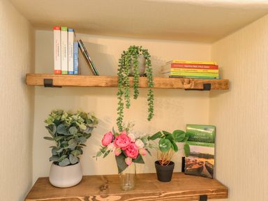 Wooden shelves with books and potted plants in a corner at Primrose Cottage Ambleside