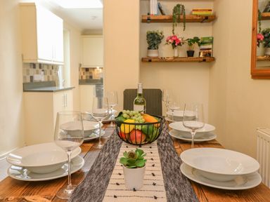 A dining table set with white plates wine glasses and a bowl of fruit in a kitchen dining area at Primrose Cottage in Ambleside