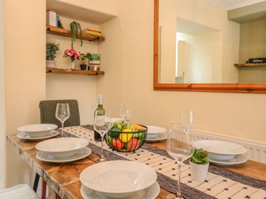 A dining table set with plates wine glasses a fruit basket and a small plant next to shelves with books and plants at Primrose Cottage in Ambleside
