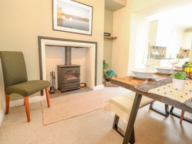 A dining area with a wood stove fireplace green chair and a wooden dining table with glassware at Primrose Cottage in Ambleside