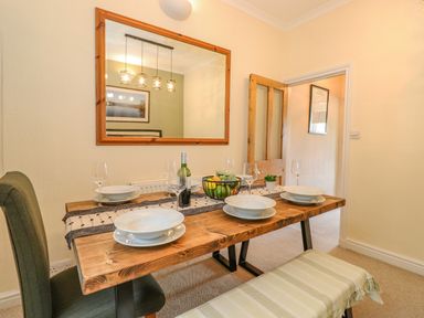 A dining room with a wooden table set with plates glasses and a fruit basket at Primrose Cottage Ambleside