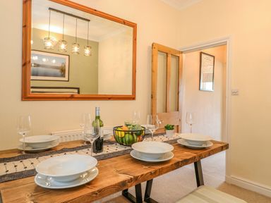 A dining area with a wooden table set with white plates wine glasses a fruit bowl and a bottle at Primrose Cottage in Ambleside