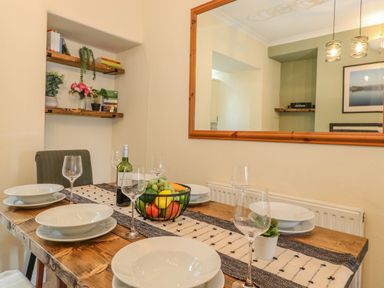 A dining area with a wooden table set with plates wine glasses and a bowl of fruit at Primrose Cottage Ambleside