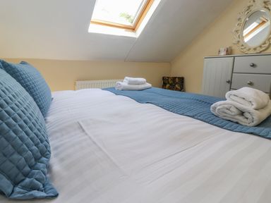 A bedroom with a bed with white sheets and blue pillows and towels on the bed under a skylight window at Primrose Cottage in Ambleside