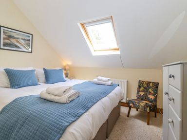 A bedroom with a double bed blue pillows folded towels a small patterned chair a white chest of drawers and a skylight window at Primrose Cottage Ambleside