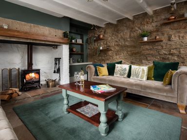 A living room with a fireplace a beige sofa with cushions a wooden coffee table and stone walls at Owl Cottage in Morpeth