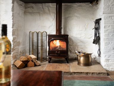 A wood-burning stove with firewood and fireplace tools in a white brick fireplace at Owl Cottage in Morpeth