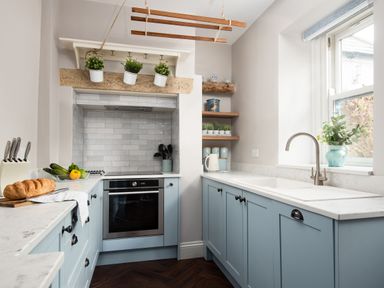 A kitchen with blue cabinets white countertops a built in oven and a window with plants on the sill at Owl Cottage in Morpeth