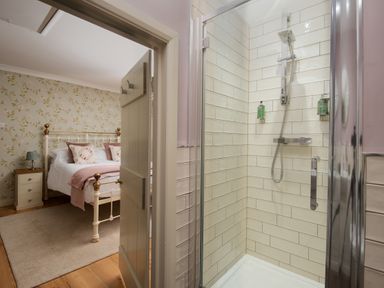 A view of a bedroom with a bed and nightstand seen through an open door next to a shower cubicle with tiled walls at Owl Cottage in Morpeth