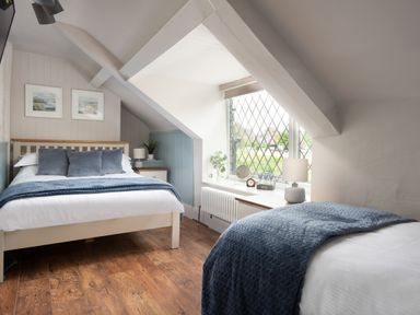 A bedroom with two beds a window with diamond patterned glass and wooden floor at Owl Cottage in Morpeth