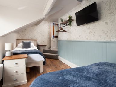 A bedroom with two single beds bedside table lamp wall mounted tv and a door at Owl Cottage in Morpeth
