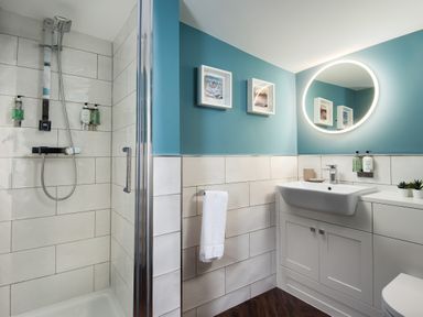 A bathroom with a shower area a sink with cabinet a round mirror and two framed pictures at Owl Cottage in Morpeth
