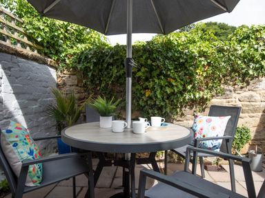 A patio table with an umbrella surrounded by four chairs with cushions and plants at Owl Cottage in Morpeth