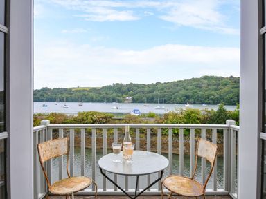A balcony with chairs and a table overlooking a waterfront at Island House in Golant near Tywardreath