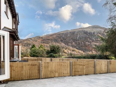 A view of a mountainous landscape behind a wooden fence from a paved patio at Hebog in Beddgelert