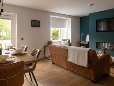 A living room with a brown leather sofa a wooden dining table with brown chairs and a wall mounted television at Hebog in Beddgelert