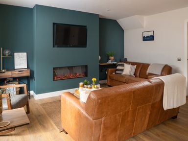 A living room with brown leather sofas a wall mounted television and a fireplace at Hebog in Beddgelert
