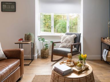 A living room corner with a leather sofa wooden side table plants a gray armchair with a cushion and a round wooden coffee table with a tray of snacks and books at Hebog in Beddgelert