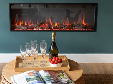 A wooden table with a tray of six champagne glasses a bottle and a bowl of strawberries in front of a modern fireplace at Hebog in Beddgelert