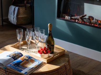 A wooden table with six empty glasses a bottle of champagne and a bowl of strawberries in front of a fireplace at Hebog in Beddgelert